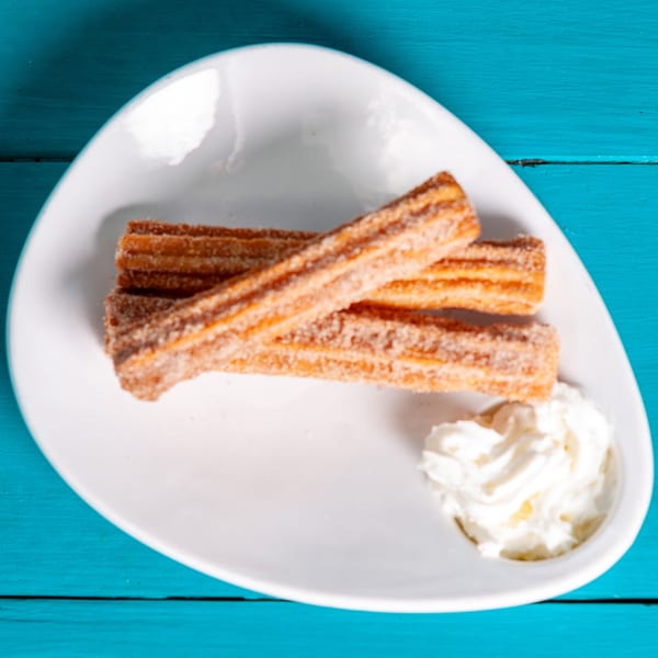 JoVi's Tacos churros, sprinkled with cinnamon sugar, served with whipped cream on a white plate.