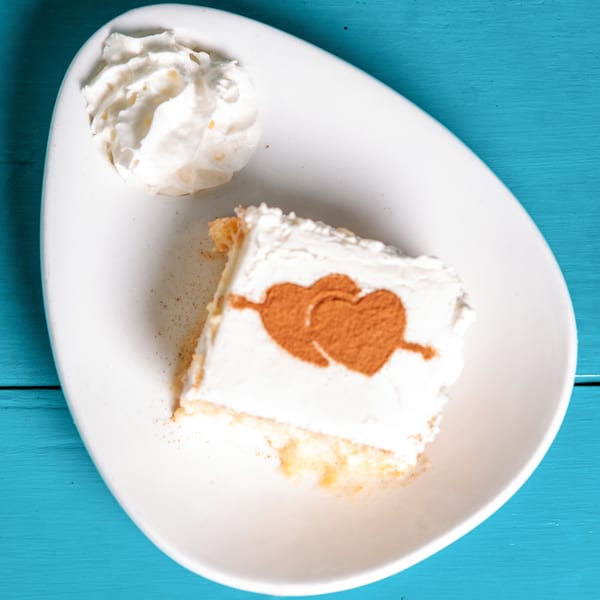 A slice of tres leches cake with whipped cream and cinnamon hearts on a white plate.
