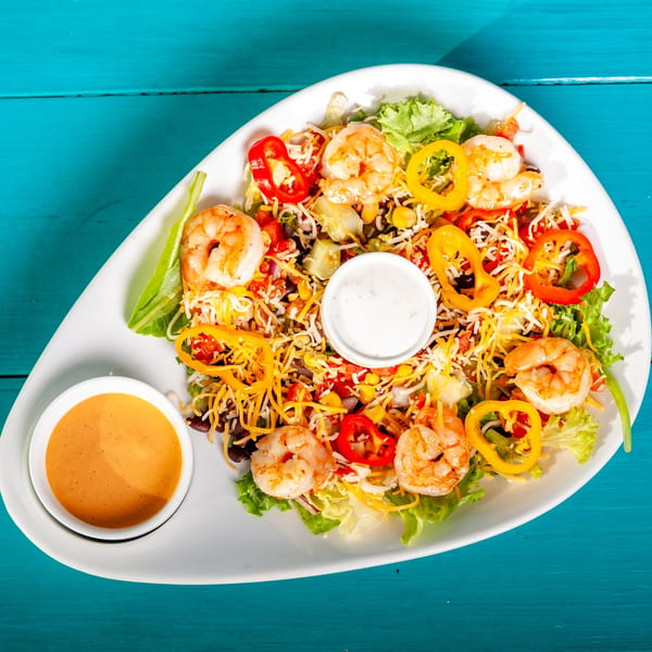 JoVi's Tacos shrimp salad with colorful vegetables, cheese, and two sauces on a blue table.