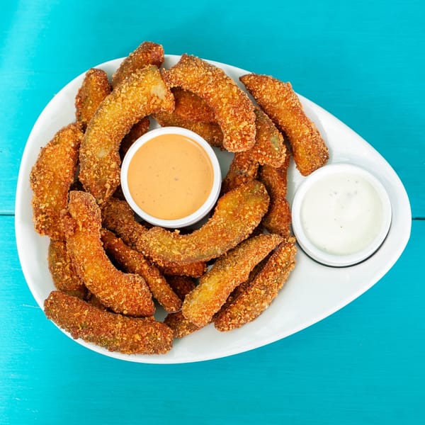 A white plate filled with crispy fried avocado slices and two dipping sauces on a blue background.