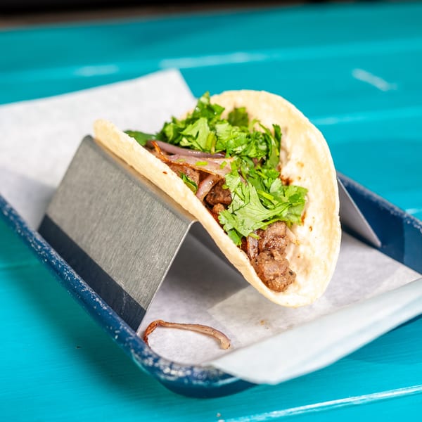 A JoVi's Tacos carne asada taco with cilantro and onions in a metal holder.