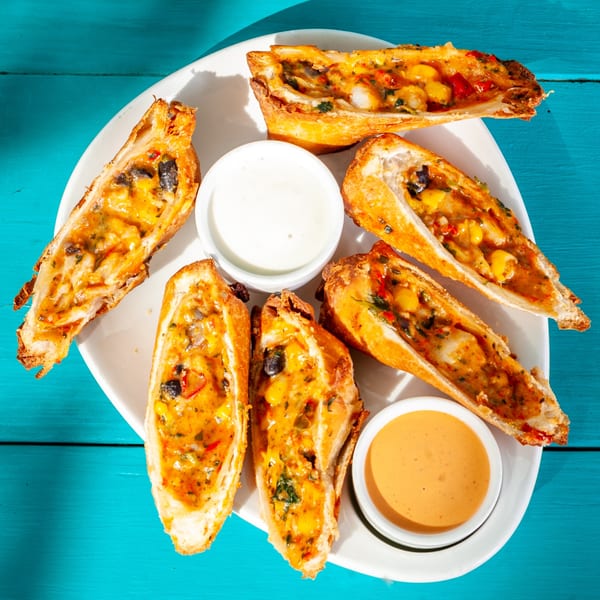 Six JoVi's Tacos boat-shaped appetizers filled with cheese, corn, and peppers, with two dipping sauces.