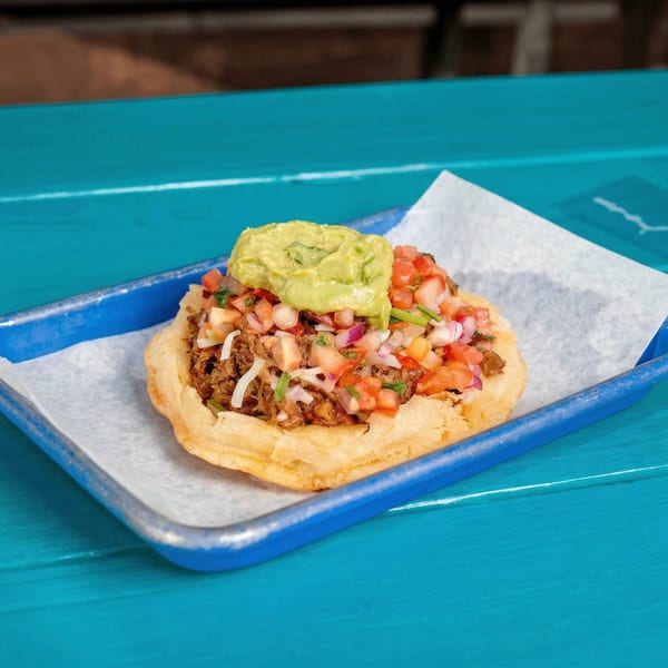 A JoVi's Tacos fried taco shell filled with meat, pico de gallo, and guacamole on a blue tray.