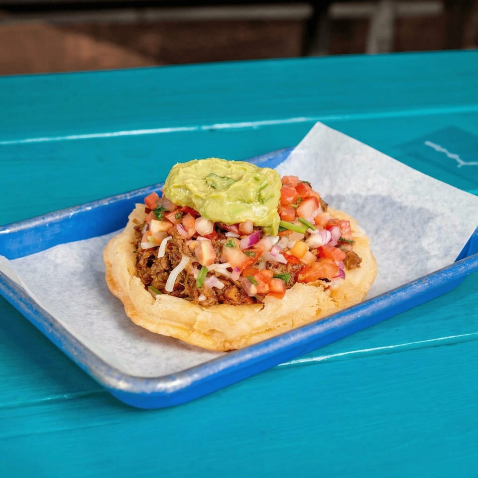 A JoVi's Tacos fried taco shell filled with meat, pico de gallo, and guacamole on a blue tray.