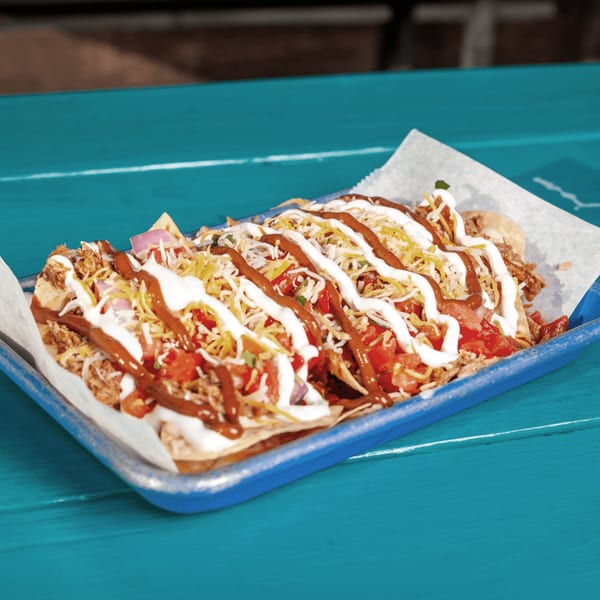 JoVi's Tacos loaded nachos with meat, cheese, tomatoes, onions, and sauces on a blue tray.